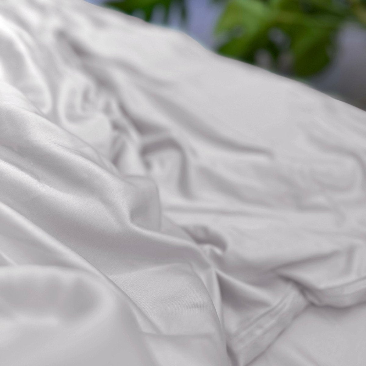 White cotton top sheet folded showing soft texture and quality fabric detail with green foliage background