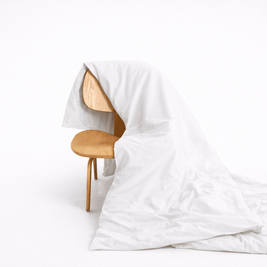 Copripiumino in bambù bianco drappeggiato su sedia in legno, mostra la trama morbida della stoffa e il design con bottoni nascosti
