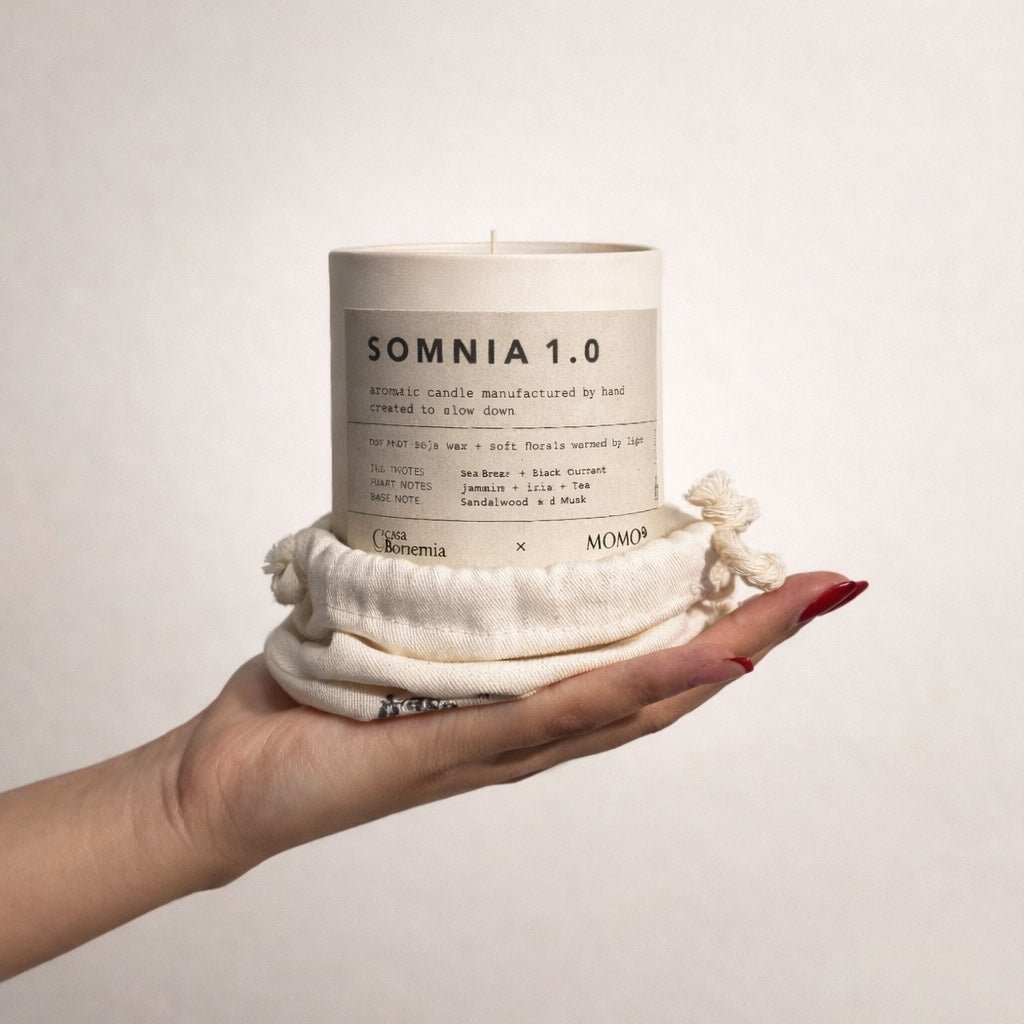 Mano che tiene candela aromatica Somnia 1.0 color crema avvolta in tessuto di cotone naturale su sfondo bianco