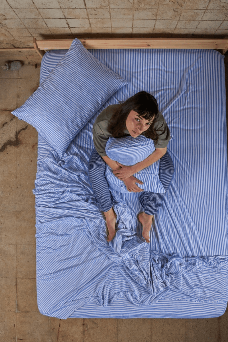 Donna distesa sul letto con set di lenzuola in cotone bambù a righe blu, vista dall'alto