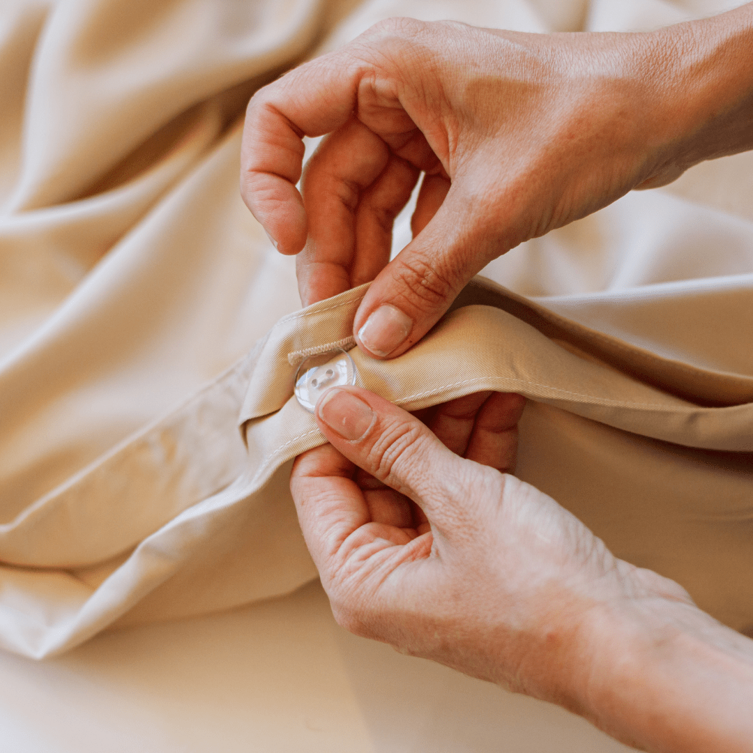 Mani che toccano la biancheria e gli asciugamani in morbido cotone beige del set completo Momo Cotton