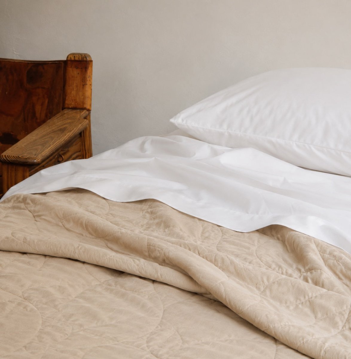 Copriletto estivo trapuntato beige su lenzuola bianche con cuscini su letto in legno