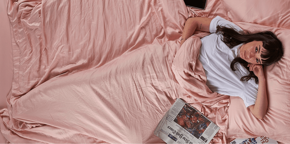 Woman lying on bed with pink bedding reading newspaper, spring bedroom décor.