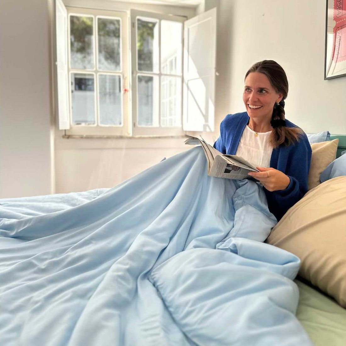 Donna a letto che legge il giornale con biancheria blu chiaro e cuscini