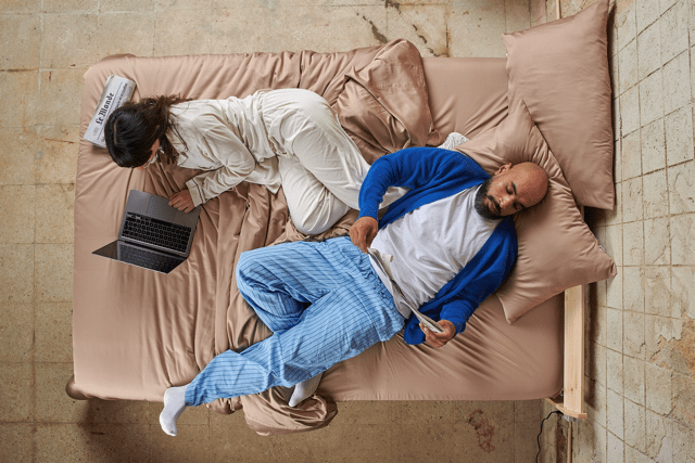 Coppia a letto con lenzuola in bambù durante il giorno, che mostra comfort in diverse stagioni.