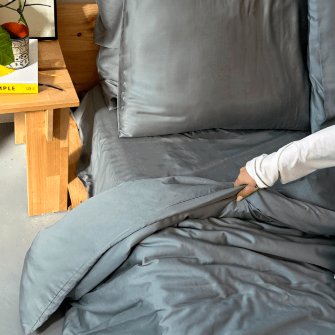 Donna che tocca la biancheria da letto in bambù grigio sul letto con tavolo in legno sullo sfondo