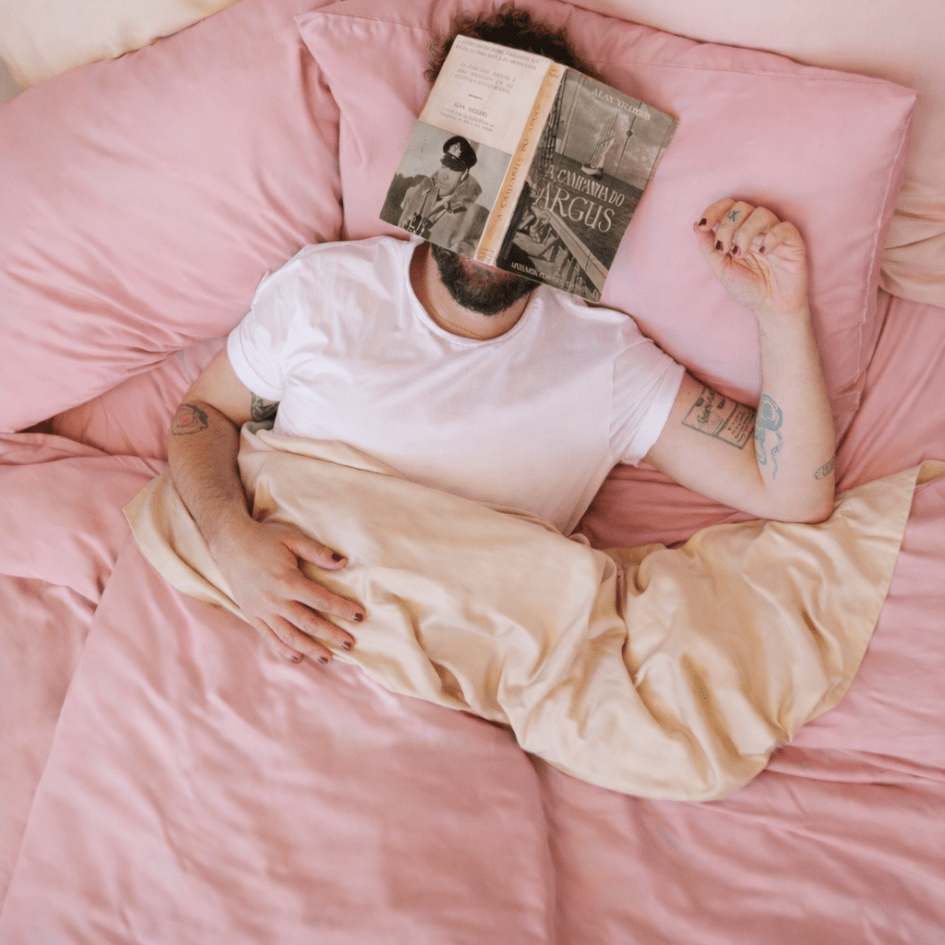 Uomo disteso su lenzuola di bambù rosa mentre legge un libro a letto