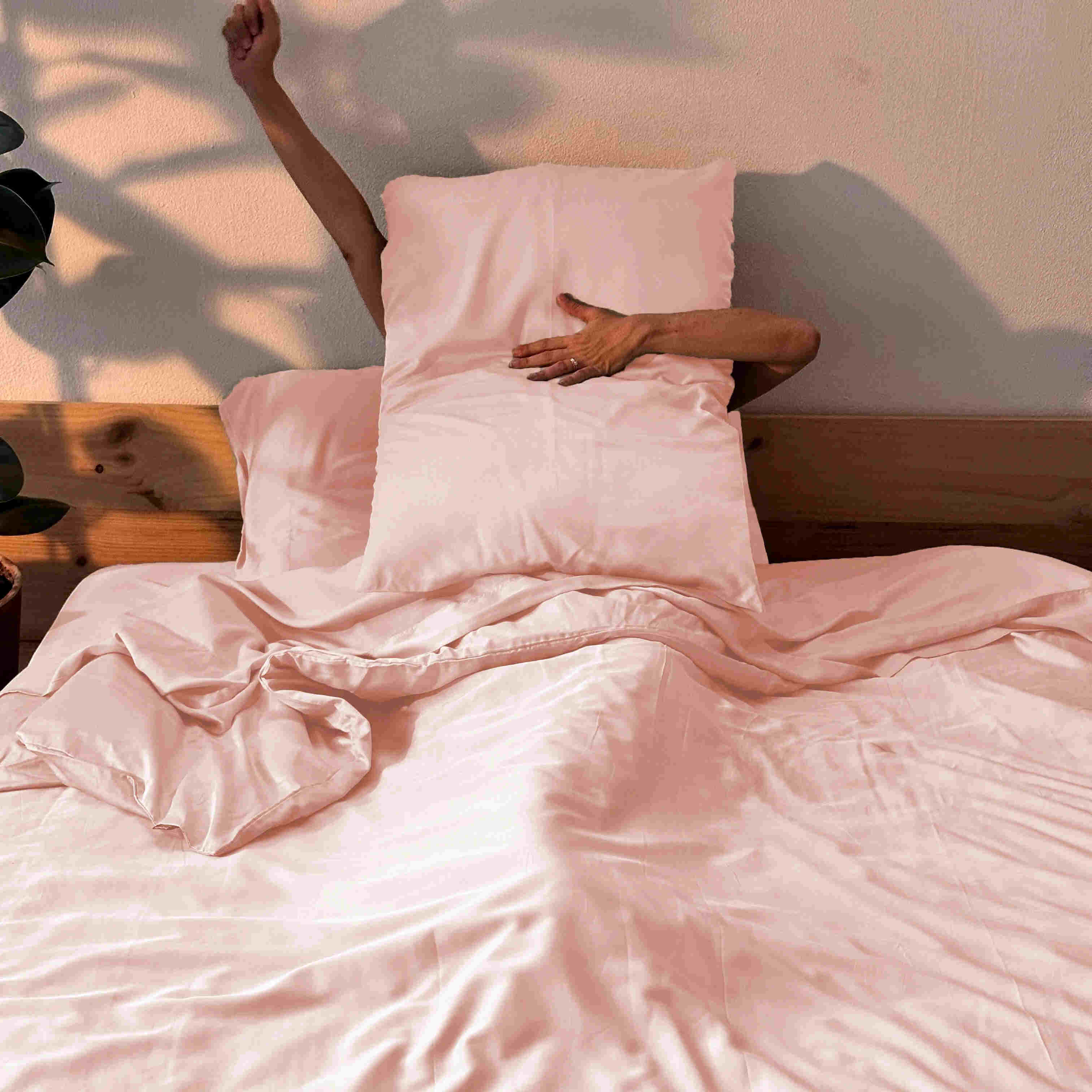 Woman in bed with pink bamboo sheets and pillows – soft, breathable and sustainable bedding