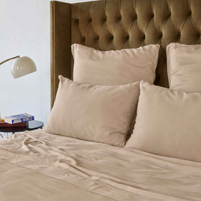 Lenzuolo superiore color crema su letto con testata imbottita marrone e cuscini beige