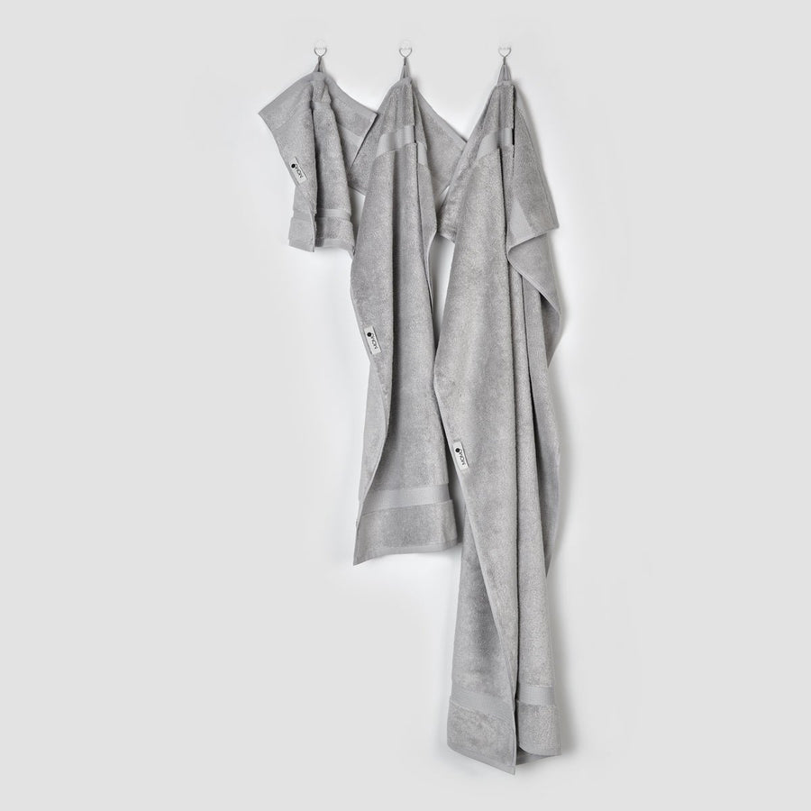 Tre asciugamani in bambù grigio appesi a ganci su sfondo bianco - asciugamani viso, mani e bagno della collezione Alba