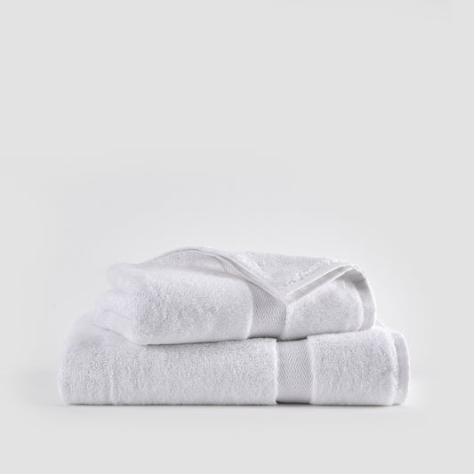 White bamboo towel set stacked on white background showing face, hand, and bath towels with woven trim detail