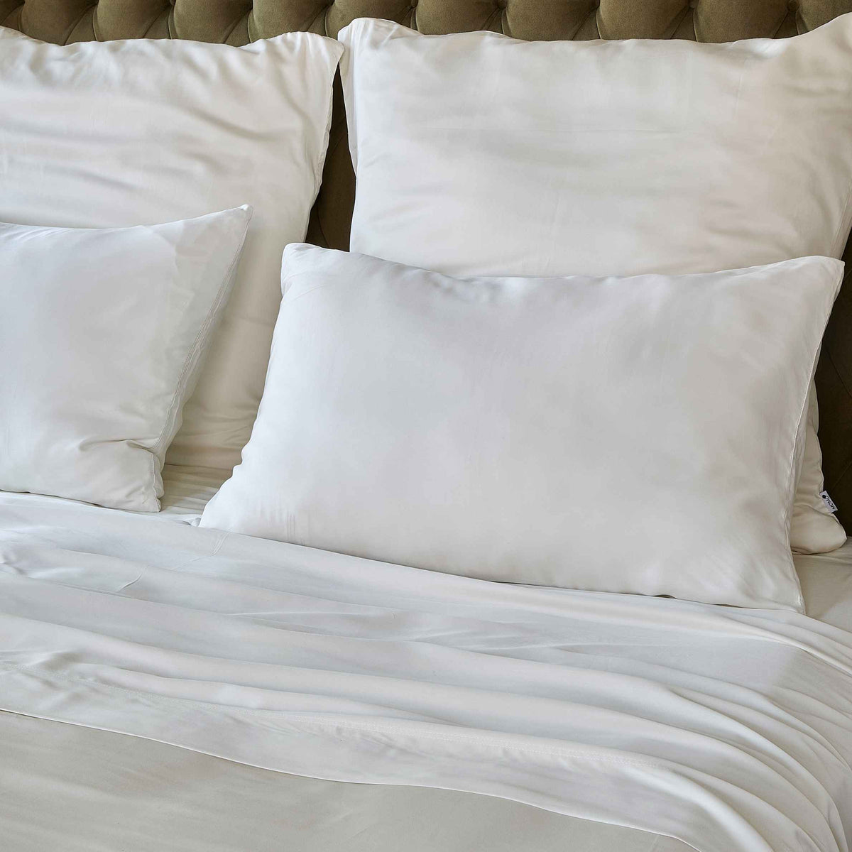 Lenzuolo bianco su letto con cuscini e testata imbottita beige