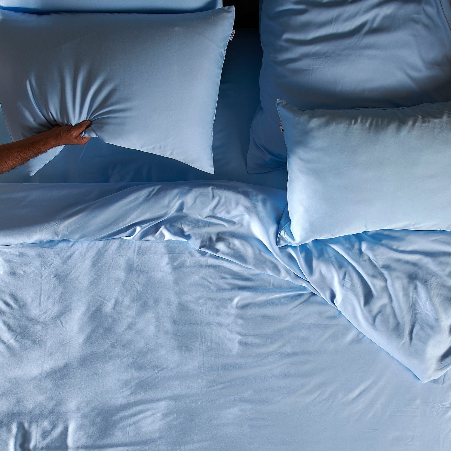 Persona che sistema il set di lenzuola in bambù azzurro con cuscini sul letto, mostrando la texture e la morbidezza