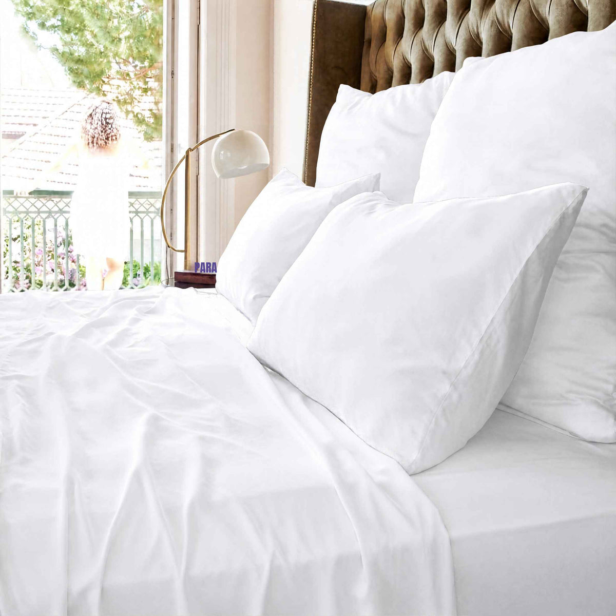 Lenzuolo bianco superiore su letto con cuscini e testata imbottita vicino a finestra con vista sul balcone