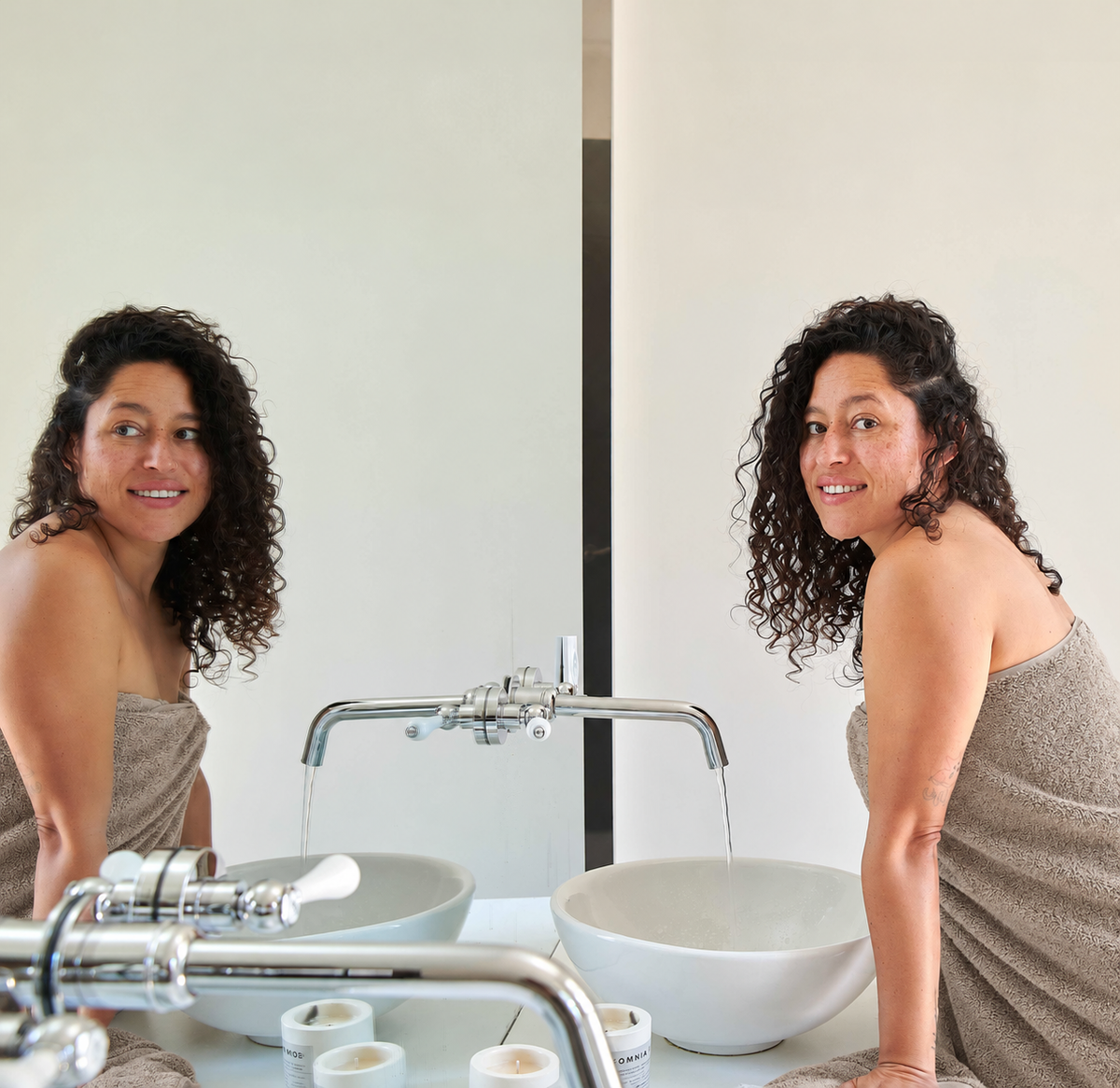 Donna avvolta in asciugamano di bambù beige davanti allo specchio del bagno