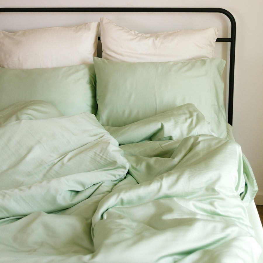 Set copripiumino verde chiaro e bianco su letto con struttura nera, decorazione con piatti in rattan a parete